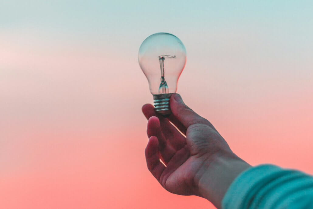 A hand holding a lightbulb in front of a blue and pink background