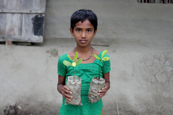 Young girl holds two mangrove saplings.