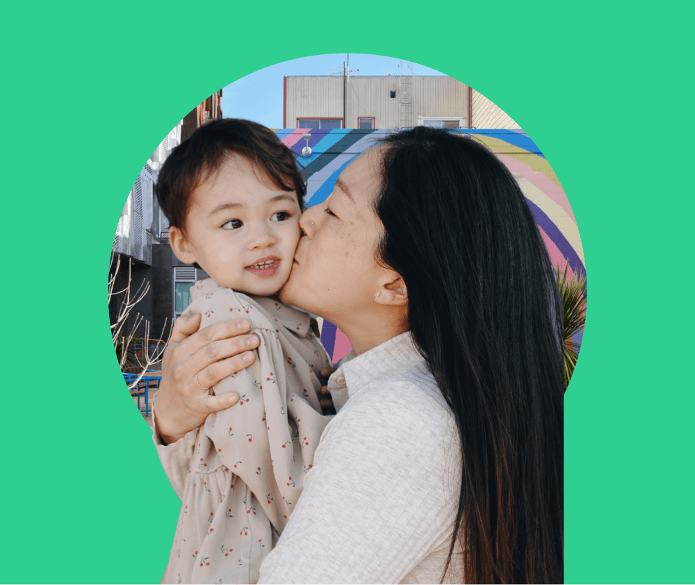 A long haired woman kissing her daughter on the cheek