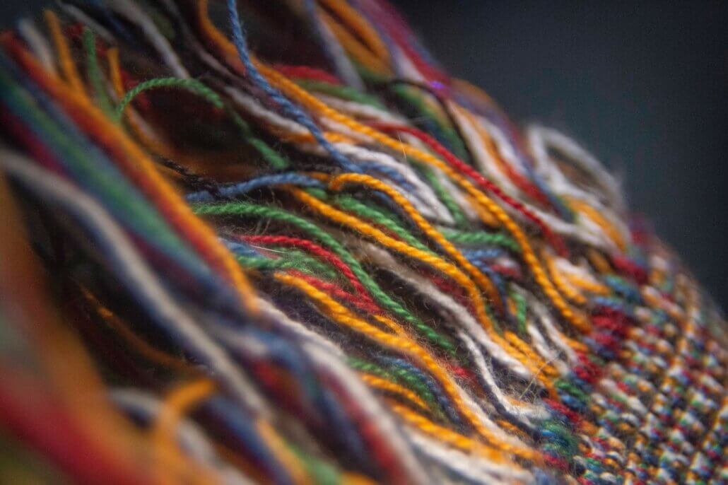 Multi-colored yarns are loose at one end and woven together to create a beautiful fabric at the other.
