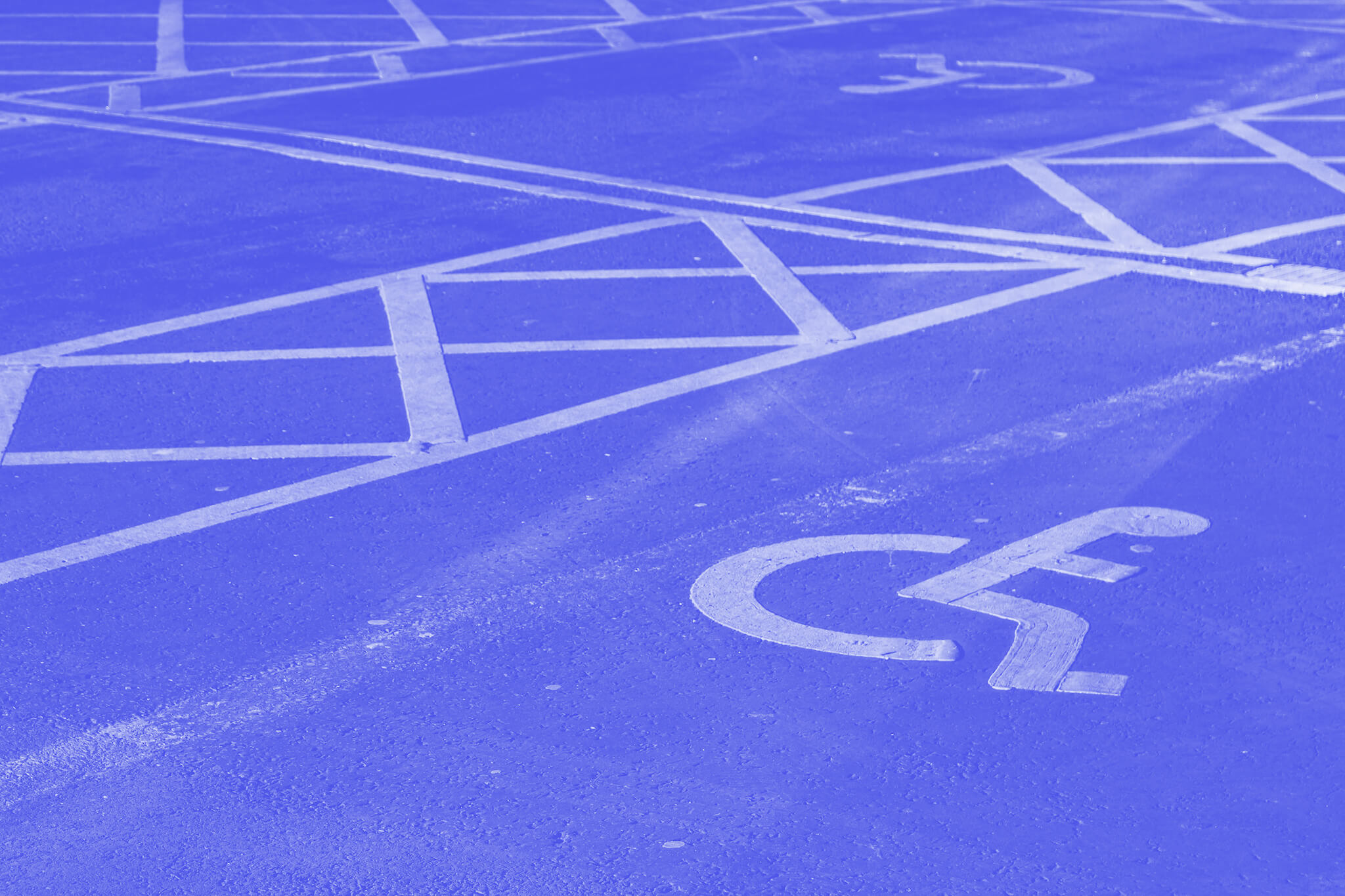 A blue parking lot with white markings including the international symbol for accessibility (wheelchair symbol)