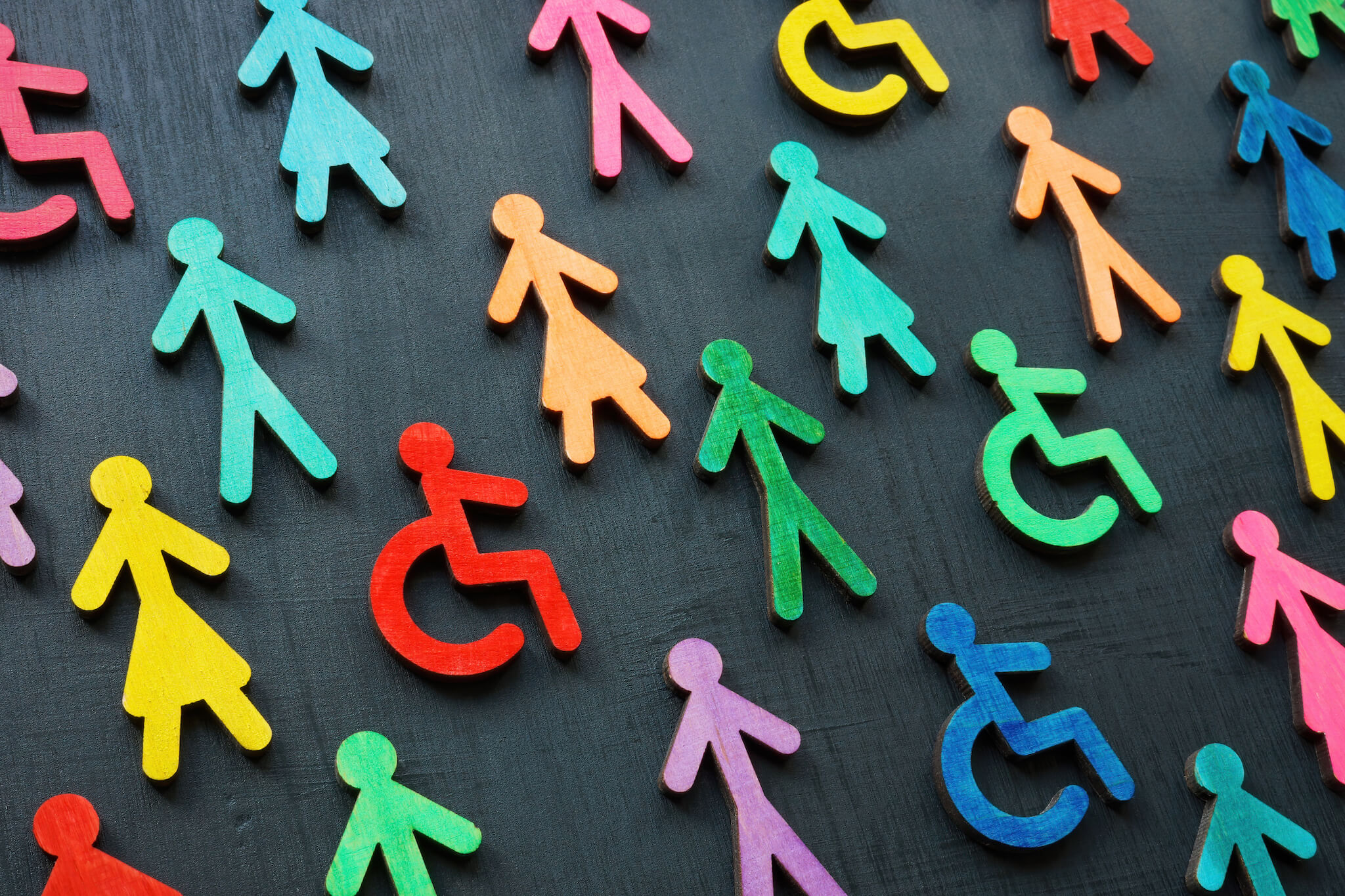 Colorful figurines of people on a dark background. Some of the figures are a person with a wheelchair.