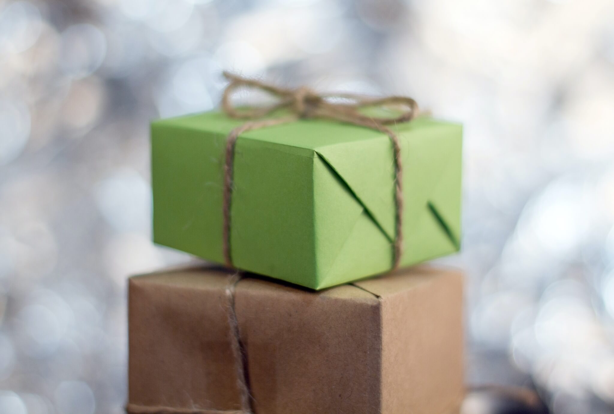 Two wrapped presents sitting on top of one another. The bottom present is wrapped in brown kraft paper. The top present is wrapped in green paper.