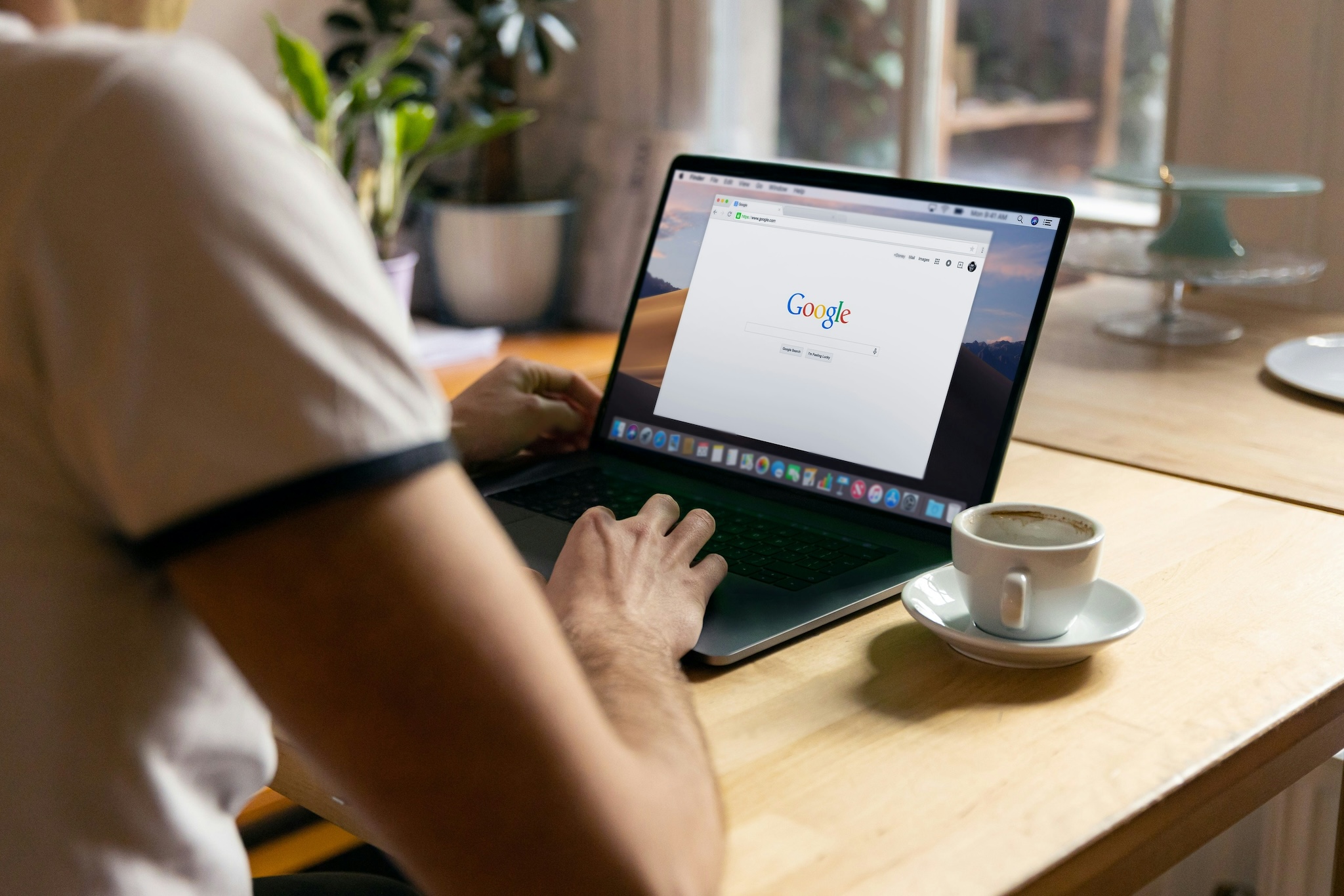 A male is using a laptop computer in a cafe or coffee shop. He is performing a search on Google.