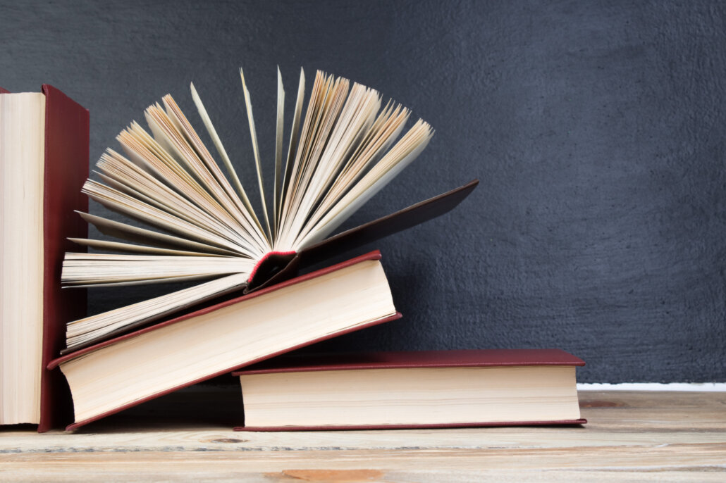 Three books placed next two each other with one open book stacked on top.