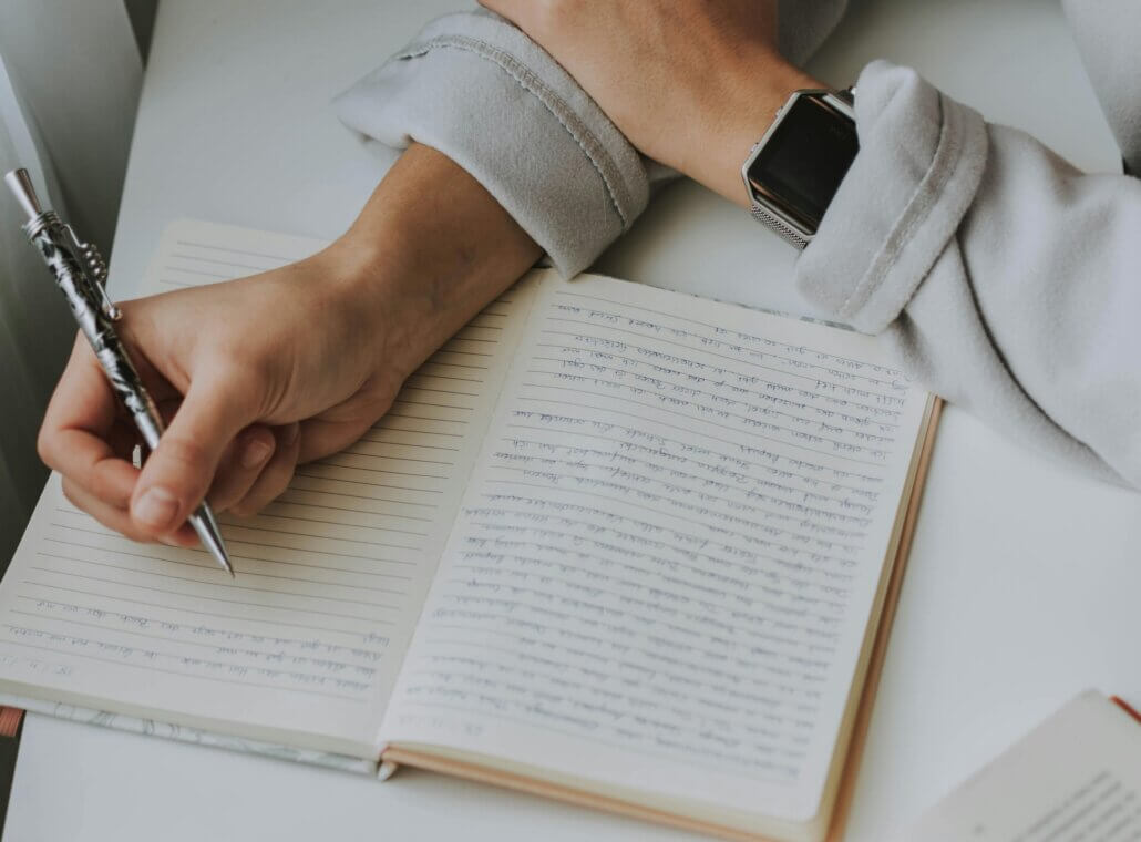 A person holds a pen and is writing in a notebook