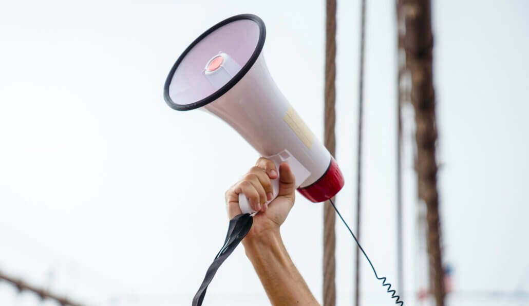 A person holding a white, black and red megaphone towards the sky.