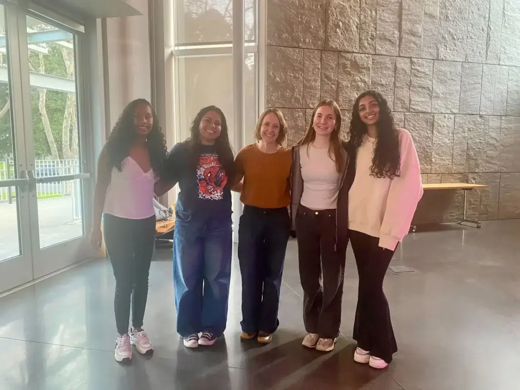 5 women standing arm in arm in a university hall